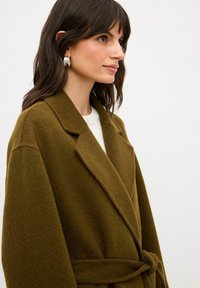 Olivgrön ull-blandad överrock med slagkrage, sidofickor och knytmidja, med en mjuk textur och avslappnad passform.