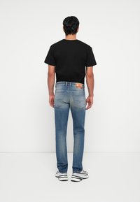 Jeans de mezclilla azul con un lavado deslavado, que presentan un diseño clásico de cinco bolsillos y una etiqueta de marca en la cinturilla trasera. Camiseta negra.