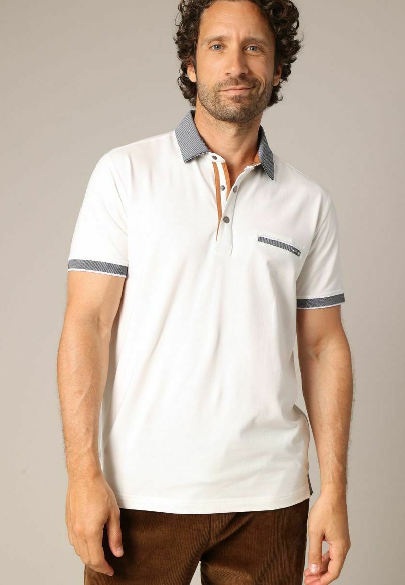 Polo-shirt blanc avec un corps uni, un col et des poignets en contraste marine, une patte de boutonnage à trois boutons et une petite poche poitrine avec un détail décoratif.