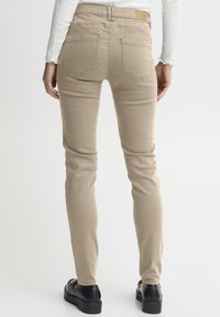Jeans skinny beiges avec une texture lisse, taille medium et poches arrière. Portés avec des chaussures à plateforme noires et un haut blanc à manches longues.