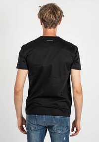Camiseta negra de manga corta hecha de algodón, con un cuello redondo y una etiqueta en la parte posterior. Combinada con unos vaqueros azules desgastados.