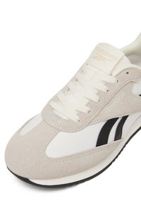 Svetlo šedé a biele tenisky so semisovými a sieťovinovými materiálmi, s čiernymi akcentmi a šnúrkami, navrhnuté s odpruženou podrážkou a logom.