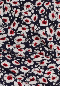Tissu bleu marine foncé avec des fleurs blanches denses, chacune ayant un centre rouge et des détails noirs, montrant des plis naturels et la texture.
