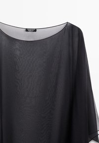 Transparent sort chiffonbluse med bred rund halsudskæring og lange ærmer, der viser lagdeling og delikate teksturdetaljer.