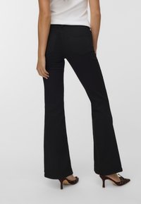 Svarta utsvängda jeans med hög midja, med traditionella bakfickor och en slät yta. Kombineras med bruna högklackade skor.