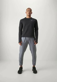 Černá mikina s dlouhým rukávem a logem Nike, v kombinaci se světle šedými joggingovými kalhotami, černými teniskami, stojící na neutrálním pozadí.