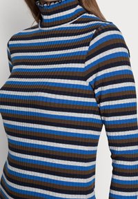Ribbad polotröja med horisontella ränder i blått, brunt och vitt. Kragen har en volangdetalj för extra textur.