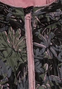 Vadderad jacka med ett mörkgrönt och svart tropiskt lövmönster, med en rosa dragkedja och hög krage. Slät yta med kontrasterande sömmar.
