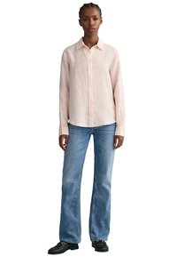 Helles rosa gestreiftes Hemd mit langen Ärmeln, kombiniert mit hellblauen ausgestellten Jeans und schwarzen strukturierten Schuhen. Einfaches, lässiges Design.