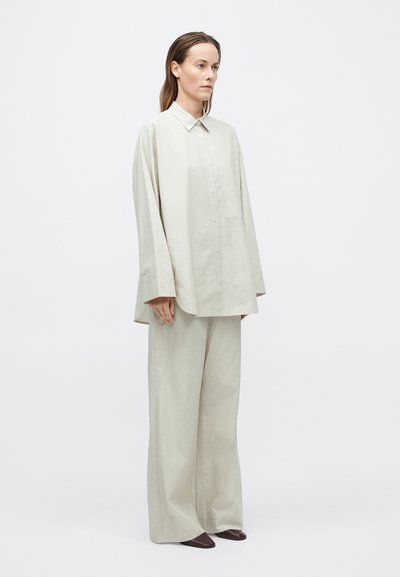 Laza szabású világosszürke ing és bőszárú nadrág, mindkettő struktúrált szövetből készült. Gombos elülső rész és egyetlen zseb az ingnél.