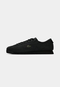 Black low-top sneaker with lace-up closure and subtle crocodile logo on the side, displayed against a white background.