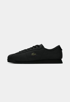 Black low-top sneaker with lace-up closure and subtle crocodile logo on the side, displayed against a white background.
