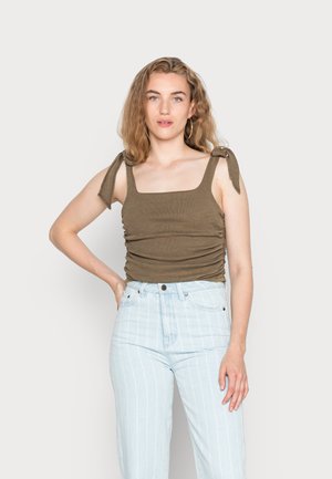 Top de tanque justo verde-oliva com decote quadrado, detalhes franzidos nas laterais e alças com laço. Combinado com jeans listrados verticais em azul claro.