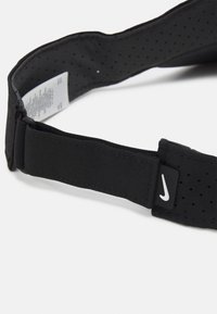 Črn elastični pas Nike z perforiranim teksturo, nastavljivo zanko in majhnim logotipnim nalepkom. Material je gladek in trpežen.