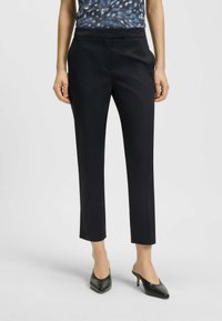 Svarta skräddarsydda byxor med slim fit, släta tyger, medelhögt midjeband och framfickor, kombinerat med spetsiga svarta klackar och en mönstrad topp.