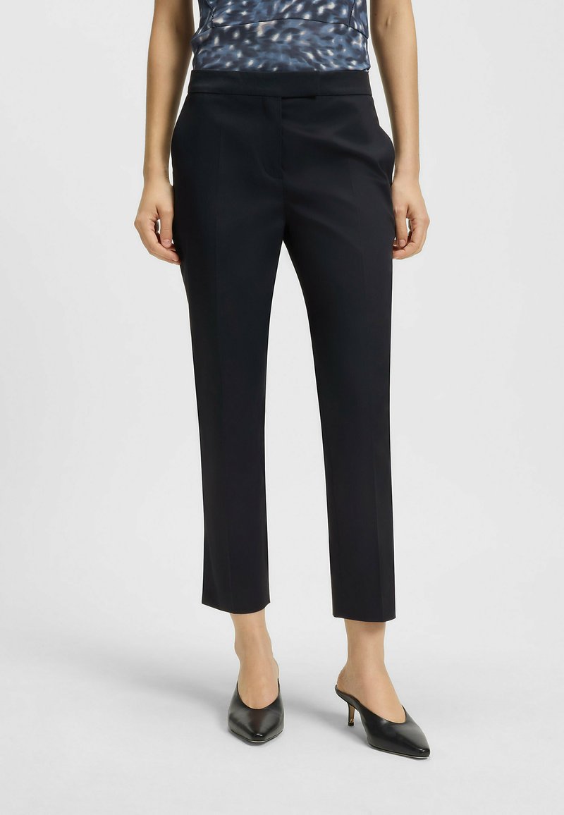 Svarta skräddarsydda byxor med slim fit, släta tyger, medelhögt midjeband och framfickor, kombinerat med spetsiga svarta klackar och en mönstrad topp.