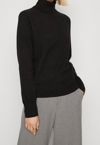 Maglione a collo alto nero in un morbido maglione a maglia testurizzata. Presenta una vestibilità slim, colletto, polsini e orlo ribattuti. Abbinato a pantaloni ampi grigi chiari.