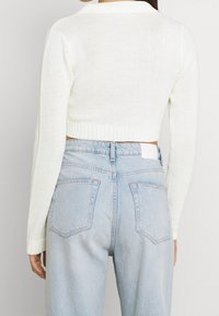 Kort vitstickad kofta med ribbad nederkant och krage, parat med ljusblå högmidjade jeans med bakfickor.