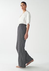 Pantaloni a palazzo in bianco e nero con motivo, caratterizzati da un'alta vita e un tessuto morbido. Abbinati a una camicia bianca dal taglio largo e sandali.