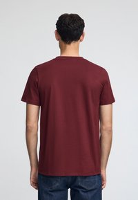 Bordeaux katoenen t-shirt met korte mouwen en een ronde halslijn, met een gladde textuur en een klassieke pasvorm, gezien vanaf de achterkant.