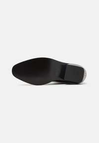 Zapato de cuero negro con una puntera suave y redondeada y diseño de tacón cuadrado. Presenta una suela plana y un sutil logotipo en la zona del tacón.