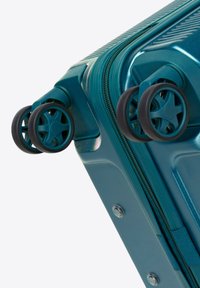 Turquoise harde koffer heeft een gestructureerd oppervlak, dubbele spinnerwielen en een ritssluiting aan de zijkant met metalen accenten.