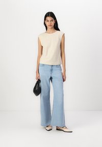 Beige ærmeløs top, lyseblå vidde jeans, sort håndtaske og flade sko i sort og beige; glatte teksturer, enkelt design.