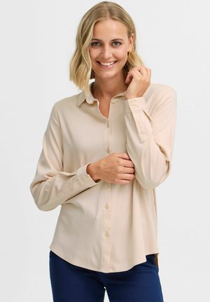Beige långärmad skjorta med knäppning i mjuk struktur, med spetsig krage och knappstängning. Slim fit med rundad nederkant.