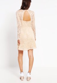 Spitzenkleid in Nude mit langen Ärmeln, offenem Rückendetail, ausgestelltem Rock, strukturiertem Blumenmuster und tailliertem Oberteil.