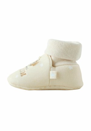 Bottines bébés beiges avec un extérieur en coton doux, un bord côtelé et une semelle texturée. Présente un design brodé et une petite étiquette sur le côté.