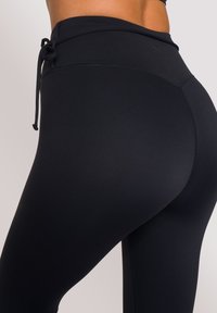 Leggings neri a vita alta realizzati in un tessuto elasticizzato, dotati di cordino e design senza cuciture, con una texture liscia e una silhouette aderente.