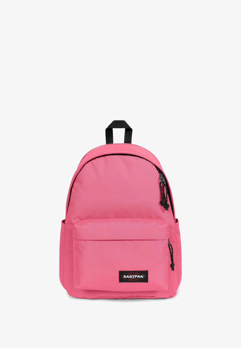 Sac à dos rose en tissu de forme arrondie, avec une poche avant, des accents de fermeture éclair noirs et une poignée de transport sur le dessus.