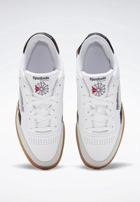 Bílé sportovní tenisky s koženým svrškem, černými akcenty, podešví z gumy, šněrovacím designem a logem Reebok na jazyku a boku.