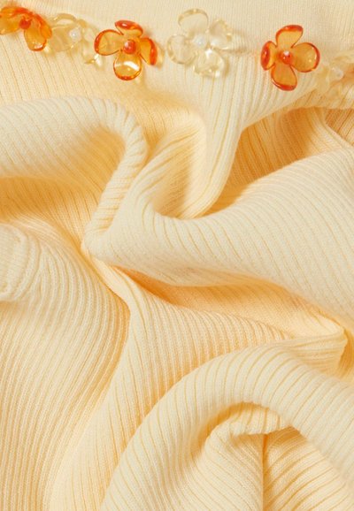 Tela acanalada de color crema con cuentas translúcidas en forma de flor naranja y transparente a lo largo del borde.