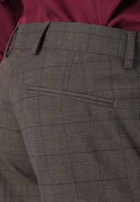 Brown checkered trousers with a textured pattern, featuring a welt pocket at the back and belt loops at the waist.