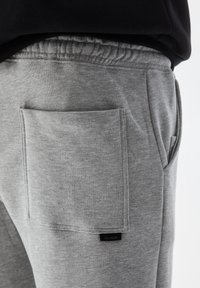 Gray cotton sweatpants featuring a large patch pocket on the right side, elastic waistband, and a small brand label near the hem.