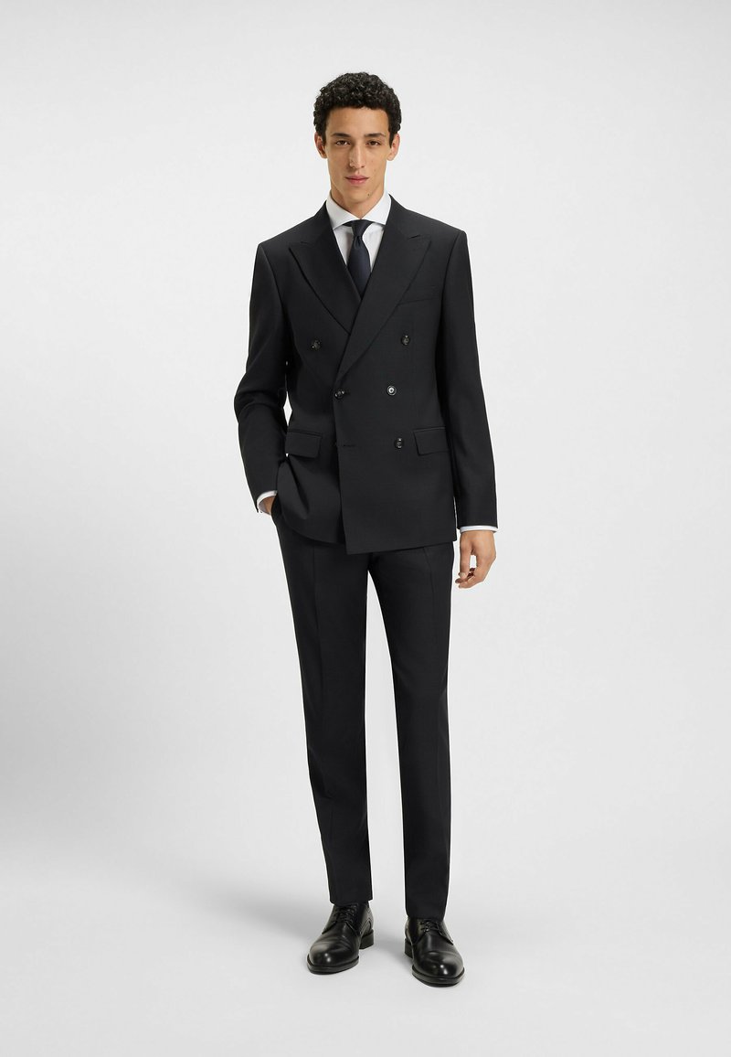 Marinblå dubbelknäppt kostym med spetsiga slag, byxor med rak front och en vit skjorta. Utrustad med svarta skor och en smal slips. Slät textur.