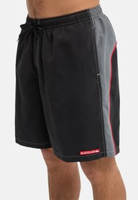 Μαύρο μαγιό βερμούδα με γκρι πλευρική λωρίδα, κόκκινη λεπτομέρεια, ελαστική ζώνη μέσης με κορδόνι και μικρό λογότυπο στο κάτω μέρος.