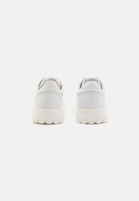Baskets blanches en cuir avec une semelle de plate-forme texturée, dotées d'un talon subtil et d'un design sans lacets. Comprend des accents gris au niveau du talon.