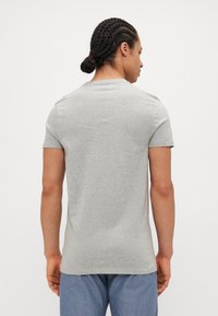 Siv majica s kratkimi rokavi iz bombaža, z znamenitim krojem in slim fit obliko. Gladka tekstura, brez vzorcev ali poudarkov.