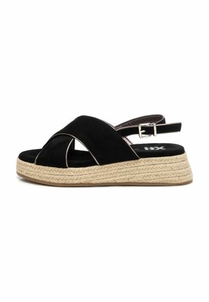 Sandalias de ante negro con tiras cruzadas, que cuentan con una suela de cuña estilo espadrille en color beige y correa ajustable en el tobillo.