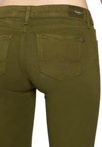 Olivově zelené Pepe Jeans s přiléhavým střihem, hladkou texturou a decentním zakřiveným prošíváním na zadních kapsách.