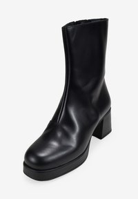 Botín de cuero negro hasta el tobillo con tacón cuadrado, textura suave, puntera redondeada y cremallera lateral para facilitar su uso. Diseño simple y elegante.