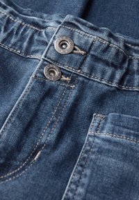 Džínové kalhoty z tmavě modré látky, s nařaseným pasem, dvěma kovovými knoflíky a viditelným švem. Obsahují detail zadní kapsy.