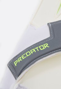 Guard sportivo bianco con cinturino grigio e la scritta "PREDATOR" in verde, superficie texturizzata e dettagli di cucitura a contrasto.
