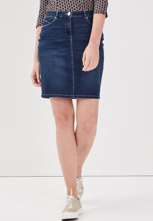 Een spijkerrok in donkerblauw met een voornaad, vijf zakken en riemlussen. Gecombineerd met beige sneakers voor contrast.