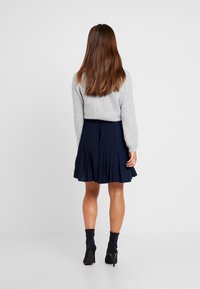 Grå stickad tröja, veckad marinblå kjol och svarta ankelboots. Bakifrån visas textur och silhuett av outfitten.