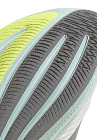 Suela de zapato que presenta una mezcla de materiales en gris y verde menta, patrones texturizados para mayor agarre y un acento amarillo brillante en el lateral.