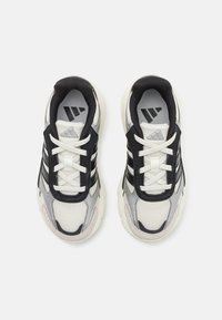 Zapatillas deportivas en blanco y negro con parte superior de malla, acentos texturizados, tres franjas negras y cordones blancos. Detalles sutiles en plata.