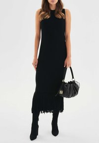 Czarna, prążkowana sukienka dzianinowa z długim, frędzlowanym dołem. Do kompletu zaokrąglona czarna torebka i czarne botki na wysokim obcasie.